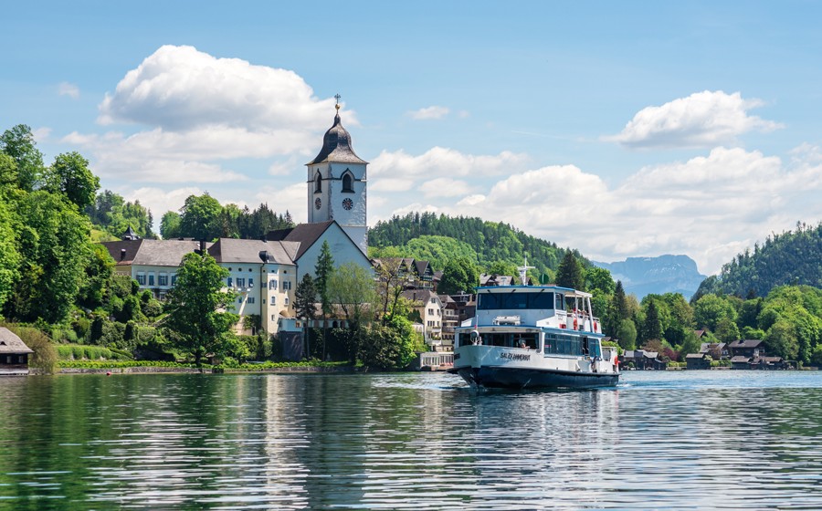 MS Salzburg auf dem Wolfgangsee im Hintergrund sieht man die Kirche von St. Wolfgang an einem sonnigen Tag mit wenigen Wolken am Himmel.