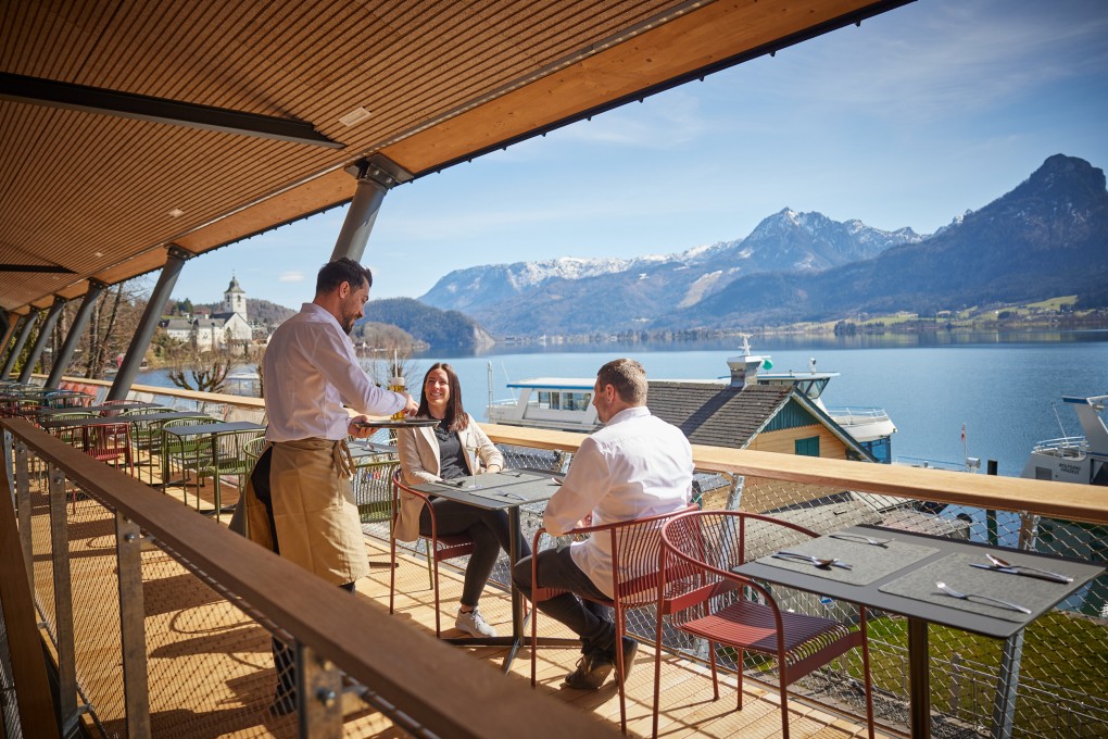 Kellner und Gäste auf der Seeterrasse des Café & Restaurant EQ mit Blick auf den Wolfgangsee 