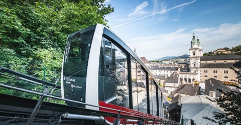 FestungsBahn fährt auf den Festungsberg mit Blick auf St. Peter Stiftskirche und Altstadt.