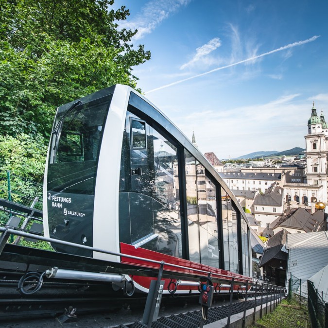 FestungsBahn fährt auf den Festungsberg mit Blick auf St. Peter Stiftskirche und Altstadt.