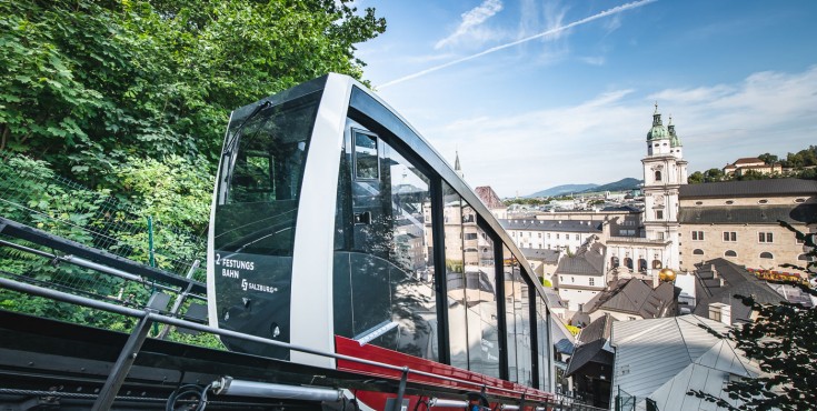 FestungsBahn fährt auf den Festungsberg mit Blick auf St. Peter Stiftskirche und Altstadt.