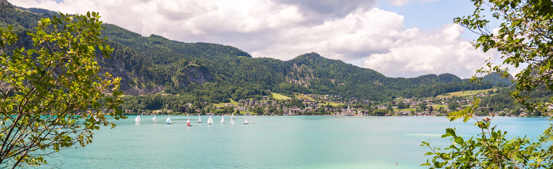 Der Wolfgangsee an einem sonnigen Tag mit viele Segelbooten, die auf dem See fahren. 