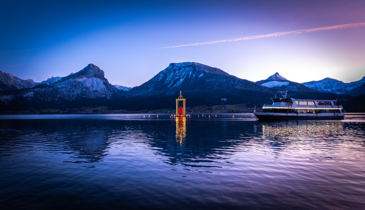 Weihnachten am Wolfgangsee. Friedenslicht am See mit einem vorbeifahrenden Schiff.