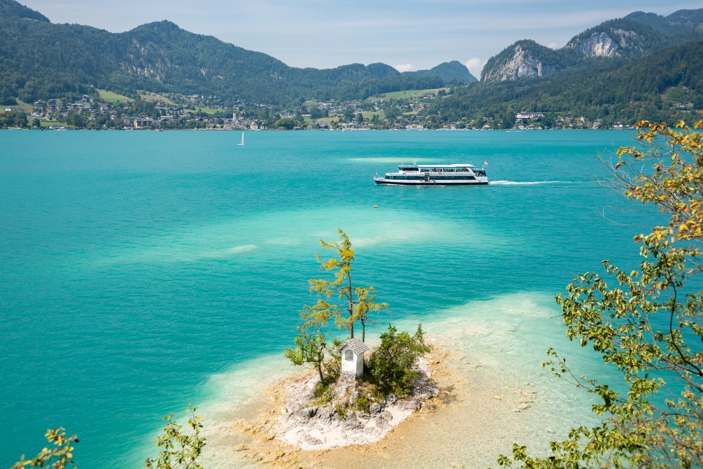 Das Schiff MS Salzburg auf dem Wolfgangsee mit einer kleinen Insel im Vordergrund wo das Ochsenkreuz drauf steht. 