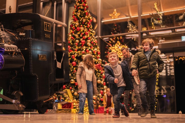 Eine Familie am Weihnachtsmarkt in der Talstation der SchafbergBahn, im Hintergrund sieht man einen festlich geschmückten Weihnachtsbaum.