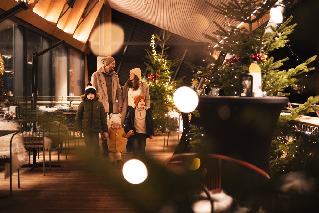 Weihnachtlich geschmückte Seeterrasse mit Weihnachtsbäumen und Fellen auf den Stühlen am Abend mit Blick auf den See. In der ferne leuchtet die Friedenslaterne auf dem Wolfgangsee