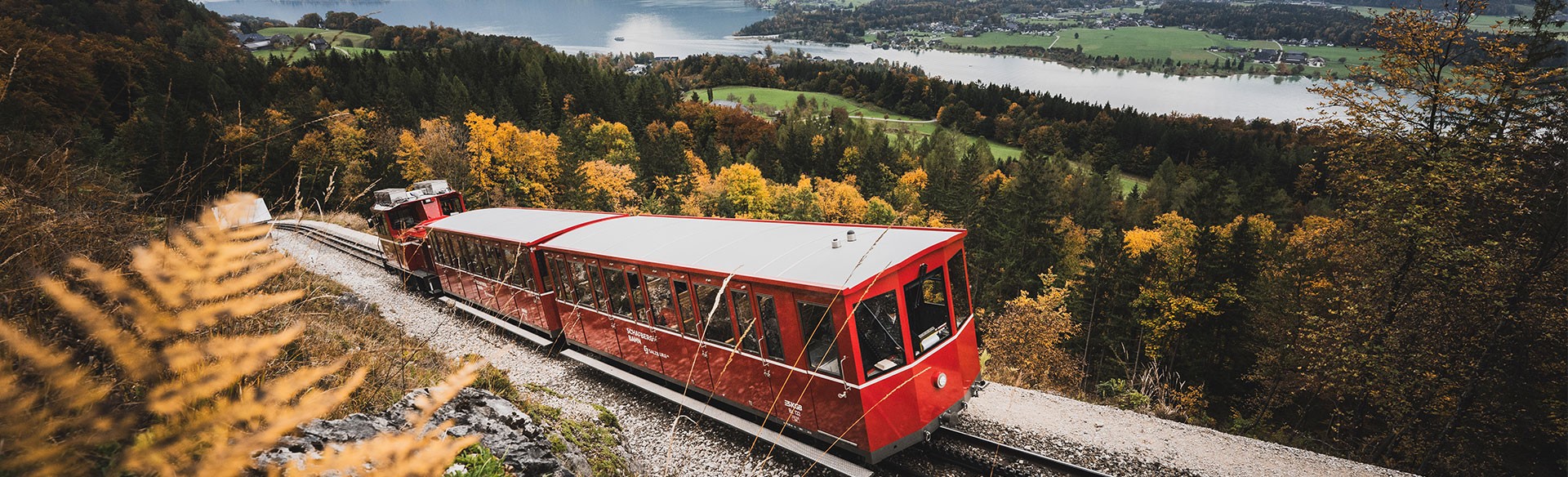 Die rote SchafbergBahn beglebt mit Weihnachtsmotiven im Herbst  auf dem Weg zum Gipfel im Hintergrund sieht man den Wolfgangsee