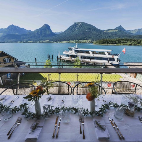 festlich gedeckter Tisch auf der Seeterrasse des Café & Restaurant EQ im Hintergrund fährt ein Schiff der WolfgangseeSchifffahrt vorbei. 