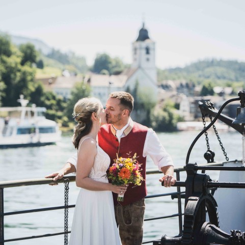 Hochzeitspaar küsst sich auf dem Schiff mit Blick vom Wolfgangsee aus auf die Kirche von St. Wolfgang