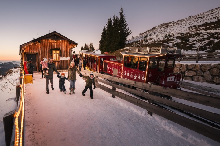 Die Schafbergalm mit der Weihnachtslok der SchafbergBahn in einer Schneelandschaft und Familie